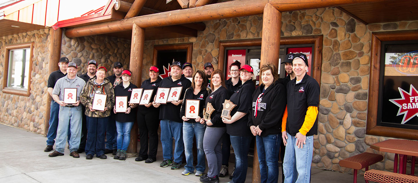 The GCM team standing together outside of the main entrance, many of the employees are holding awards they've earned
